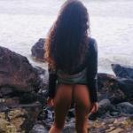 Teen with long curly hair bottomless on the rocky beach
