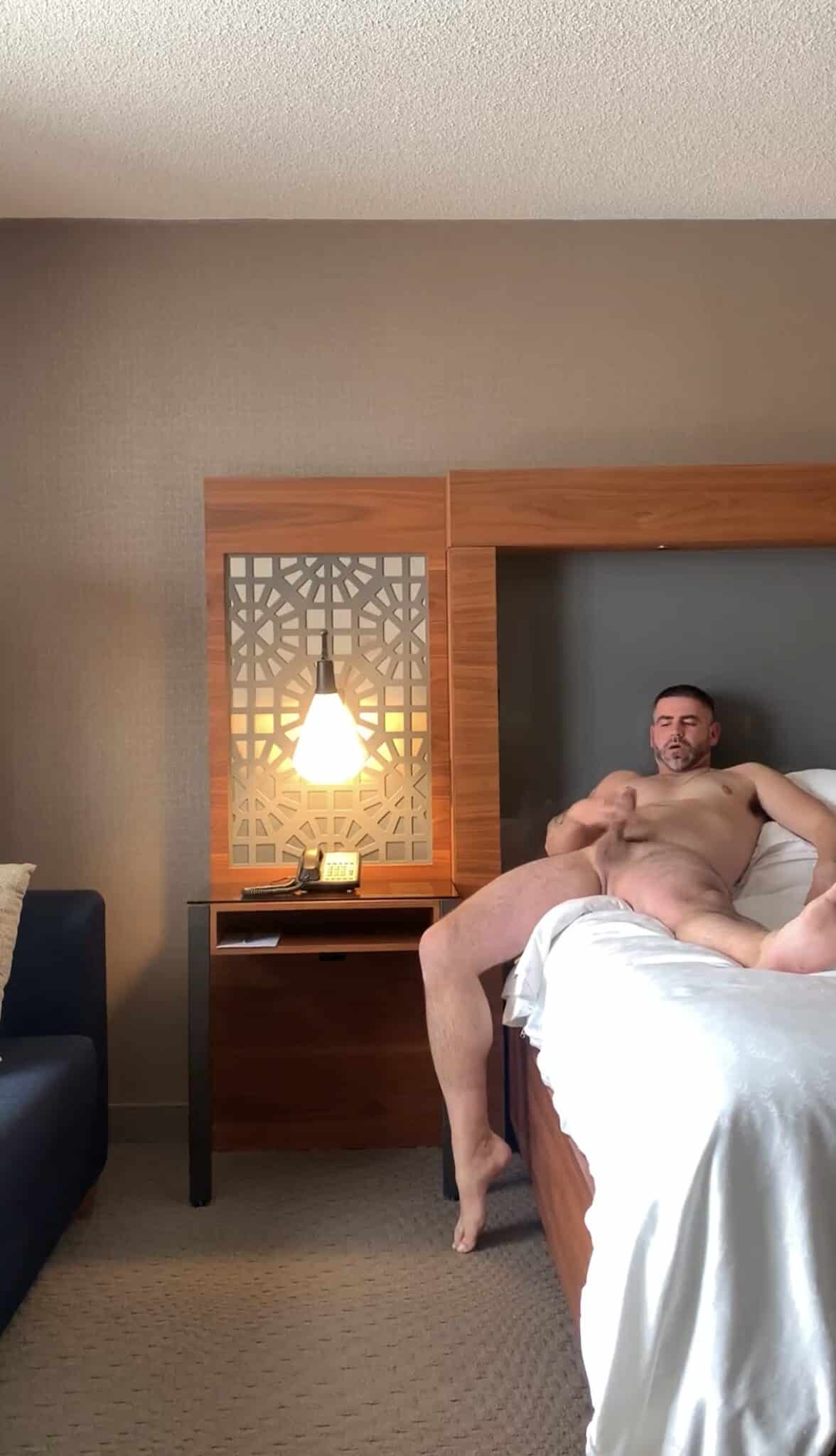 Dick Flash Pics: Bedroom Voyeur: Masturbating Alone A muscular man masturbates alone in a dimly lit bedroom, legs spread wide, lost in the moment. The scene captures a private, unfiltered glimpse of pleasure.