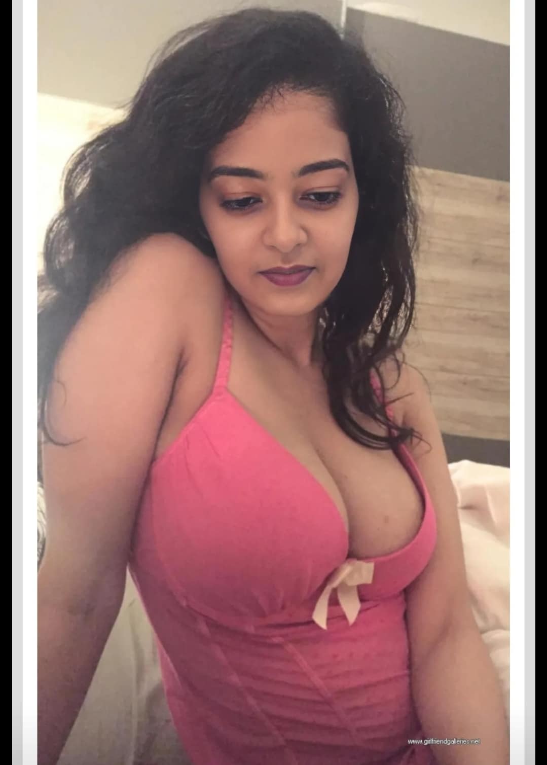 Boobs Flash Pics: Bedroom Tease: Curvy South Asian Beauty in Pink Curvy South Asian woman in a tight pink top teases with prominent cleavage and sultry gaze in a bedroom setting.