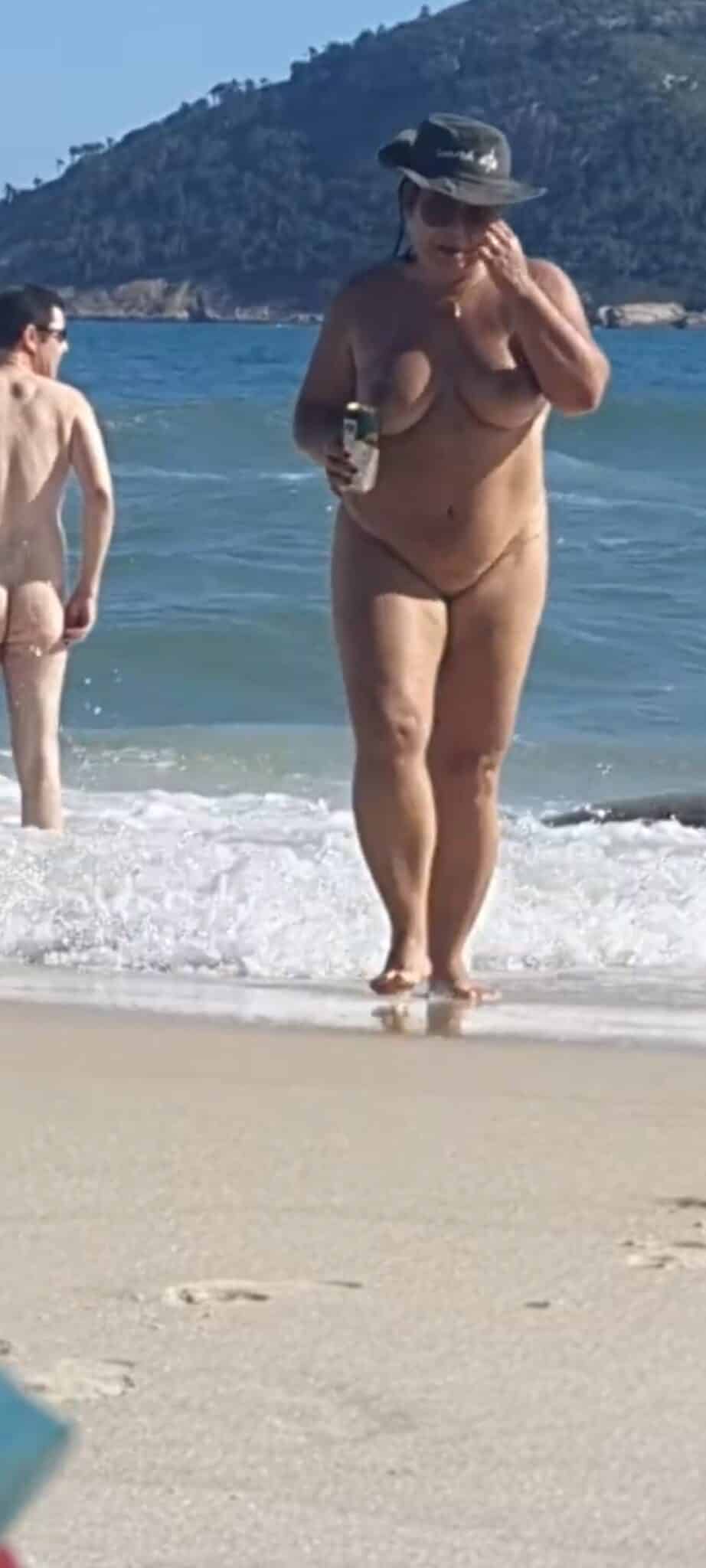 Ass Flash Pics: MILF Flashes Thong on Nude Beach A MILF in a black thong flashes her curves on a nude beach, with a man nearby fully nude, showcasing public nudity and voyeurism.